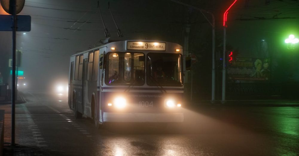 Bus Routes - Old trolleybus driving along wet asphalt road in small city at foggy night