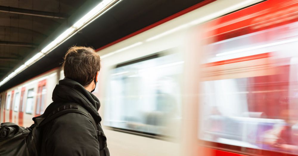 Public Transport Safety - Side view of faceless male passenger in protective mask wearing warm outerwear standing on platform of metro station near train