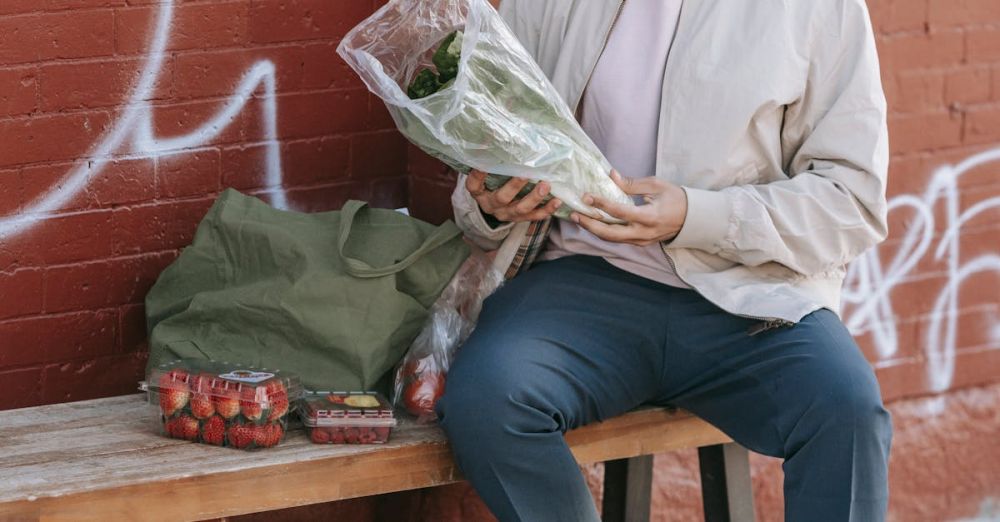 Vegan Options - Full body of young Hispanic male customer holding plastic sack with greenery while sitting on bench with cloth bag and fresh groceries after shopping