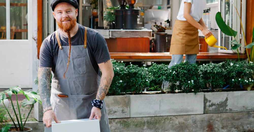 Local Designers - Happy couple of coworkers in aprons and casual clothes standing near signboard and watering plants near cafe in daytime and looking at camera