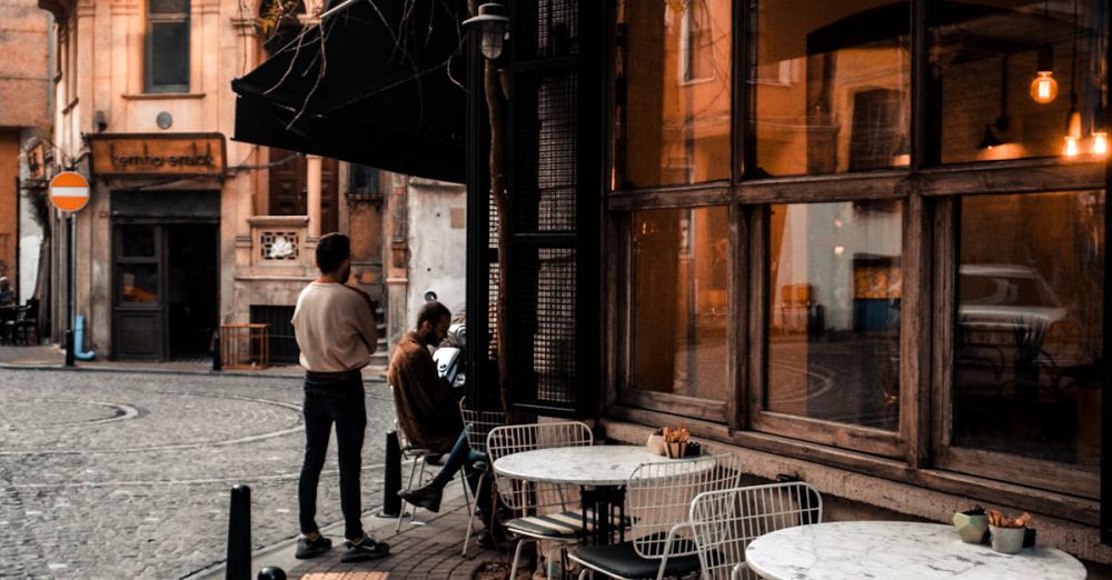 Historic Center - Facade of cafe with large windows and tables on sidewalk along road and faceless people resting in city